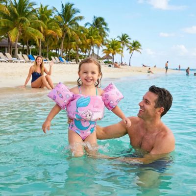 fillette avec brassard flottant dans la mer avec papa et maman assise sur le sable fait coucou