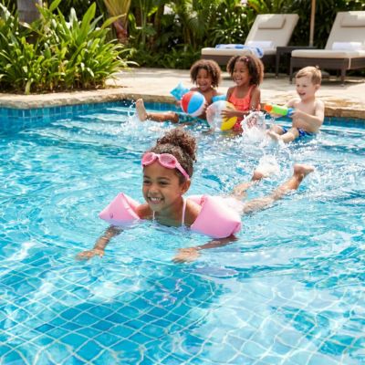 fillette avec brassard flottant entrain de nager dans piscine avec ses amis