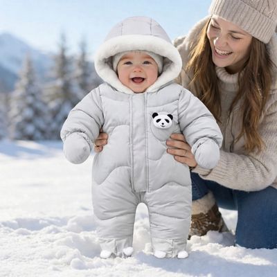 maman tenant bébé habillé avec combinaison hiver bébé debout sur neige 