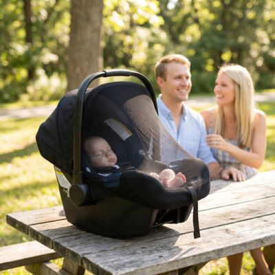 bébé dans siège auto couvert par moustiquaire poussette sur une table dans un parc avec parents