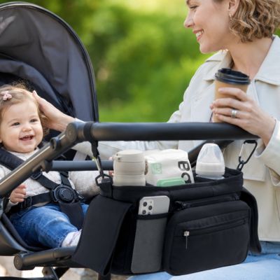 organisateur de poussette accroché par velcro sur poussette avec bébé souriant dedans et maman tenant tasse de café au parc
