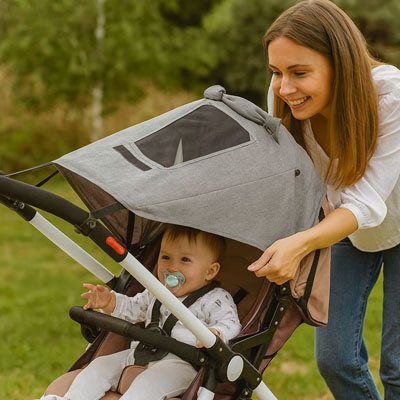 Une maman place le par soleil pour poussette sur une poussette dans laquelle se trouve bébé assis avec tétine