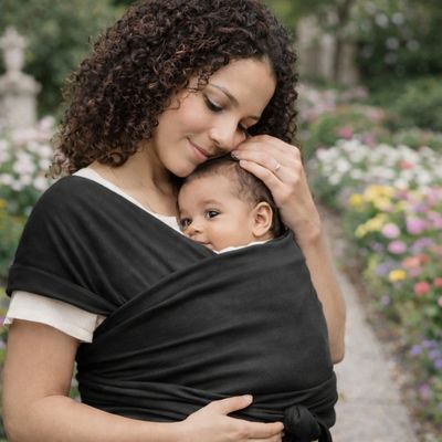 bébé porté dans porte bebe echarpe par maman aux cheveux frisés dans un beau jardin fleuri