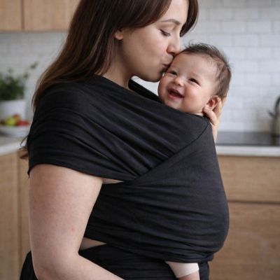 maman portant bébé dans porte bebe echarpe et lui faisant un bisous sur la tête