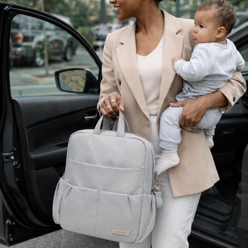 maman très élégante pourtant bébé dans le bras gauche et sac à langer sac à dos dans l'autre