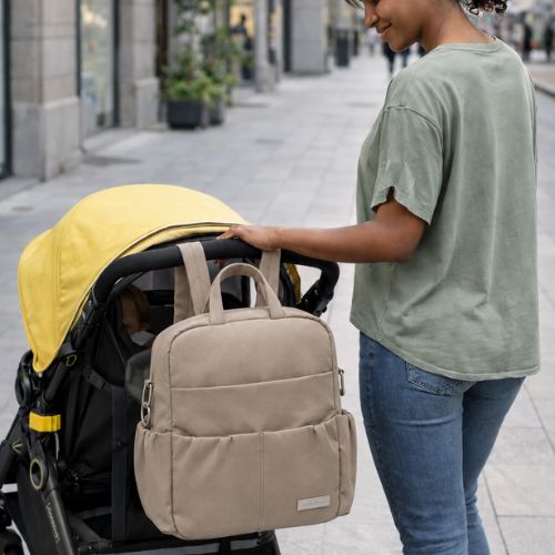 maman sur trottoir avec sac à langer sac à dos accroché à la poussette où se trouve bébé