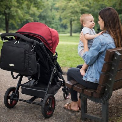 sac a dos a langer accroché à une poussette à côté de maman assise sur un banc au parc tenant bébé sur ses genoux