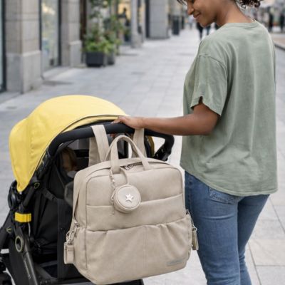 maman sur trottoir avec sac à langer sac à dos accroché à la poussette où se trouve bébé