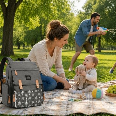 sac a dos a langer sur natte de pique nique avec maman et bebe assis et papa jouant pistolet a eau