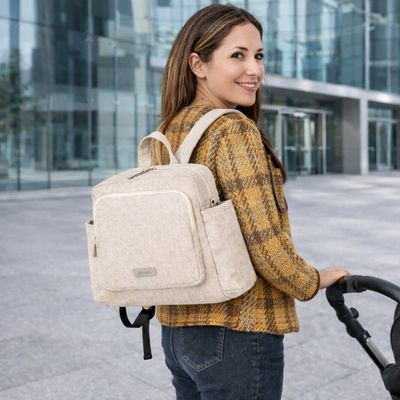 maman portant sac a dos a langer à son dos, devant grand immeuble vitré