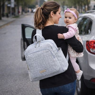 maman portant bébé dans ses bras et sac a dos a langer à son dos se dirigeant vers sa voiture