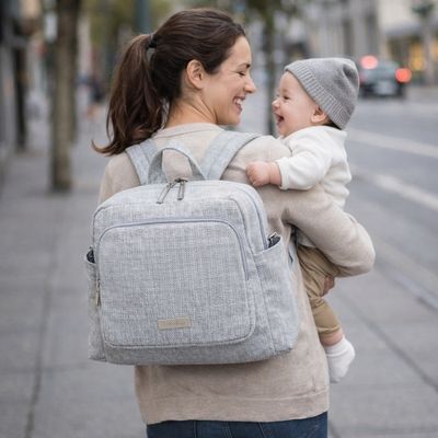 sac a dos a langer porté par maman souriant à son dos et portant bébé dans ses bras en marchant en ville