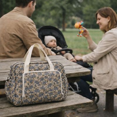 sac a langer bebe posé sur table pique nique au parc avec parents assis sur banc et bébé dans poussette