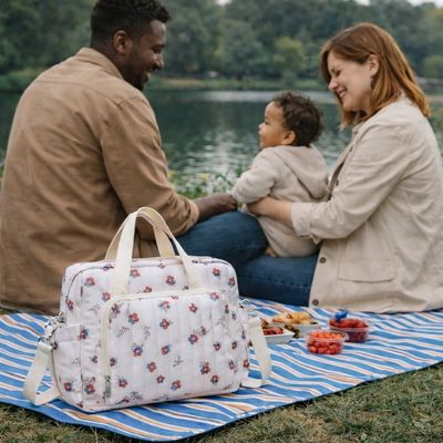 sac a langer bebe posé sur natte de pique nique au bord d'un lac avec parents et bébé heureux