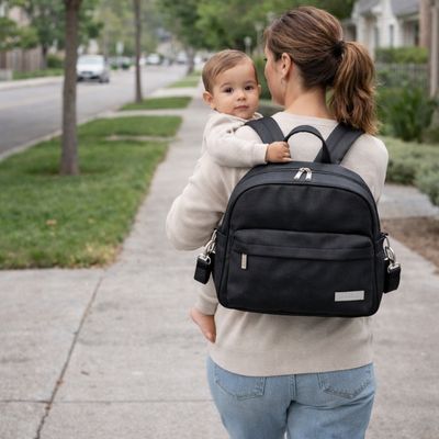 maman portant bébé aux bras entrain de marcher dans quartier avec sac à langer sac à dos à son dos